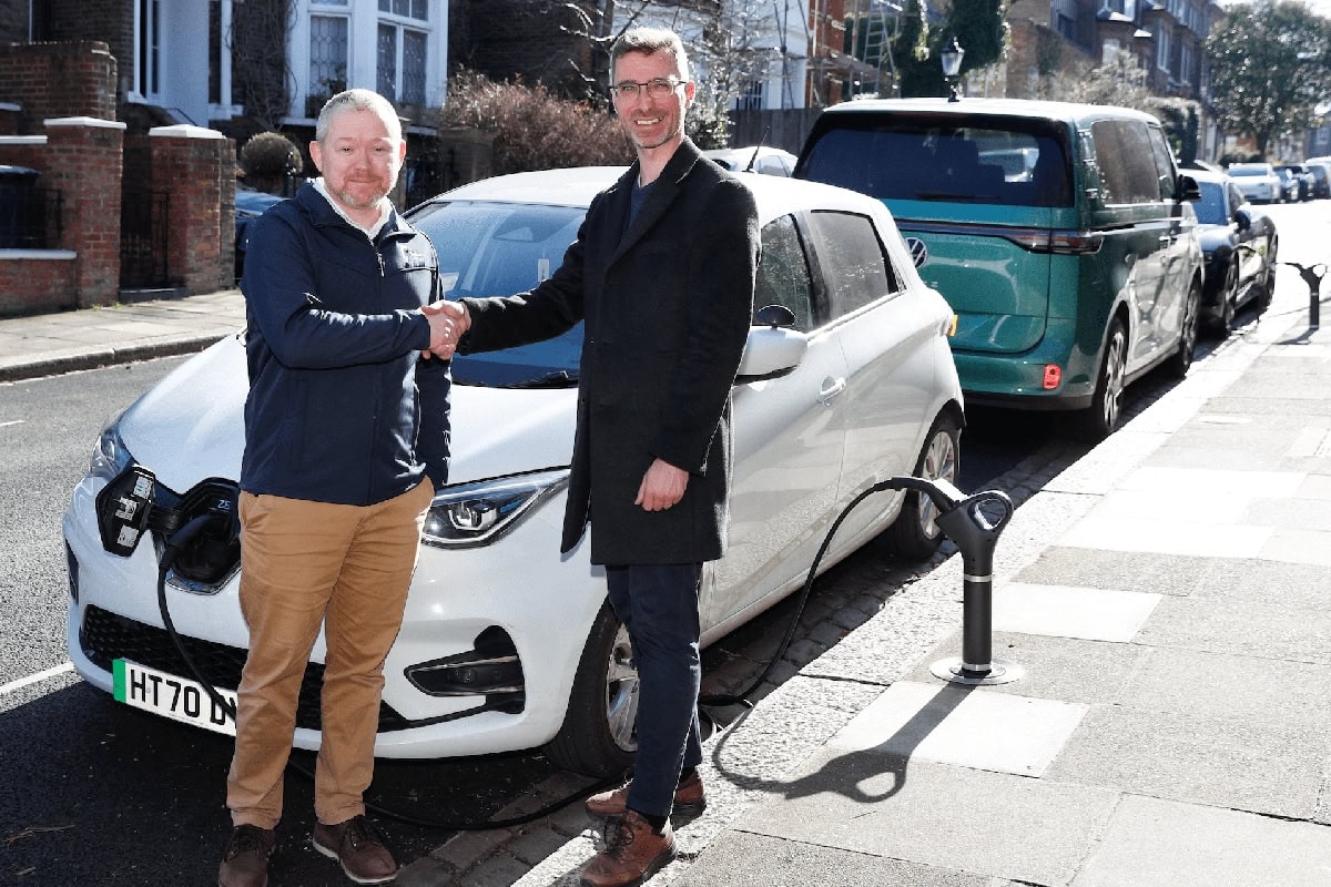 Two men shaking hands by electric car, Camden, residential street.