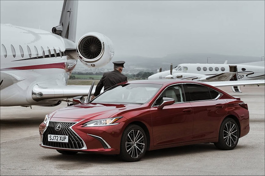 Chauffeur by a red Lexus near a private jet at the airport
